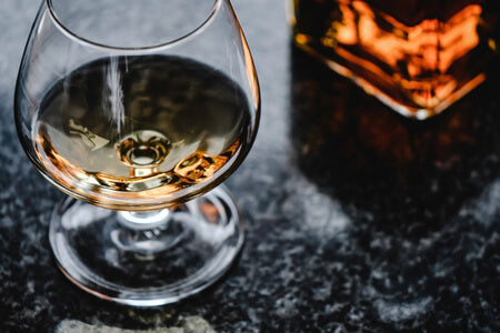 Picture of a glass of brandy on a marble table with bottle of brandy in the background